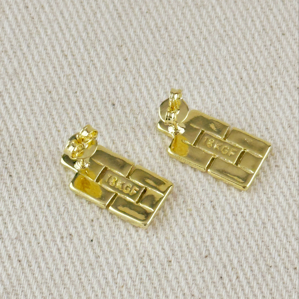 Gold bar-shaped earrings on a beige fabric background