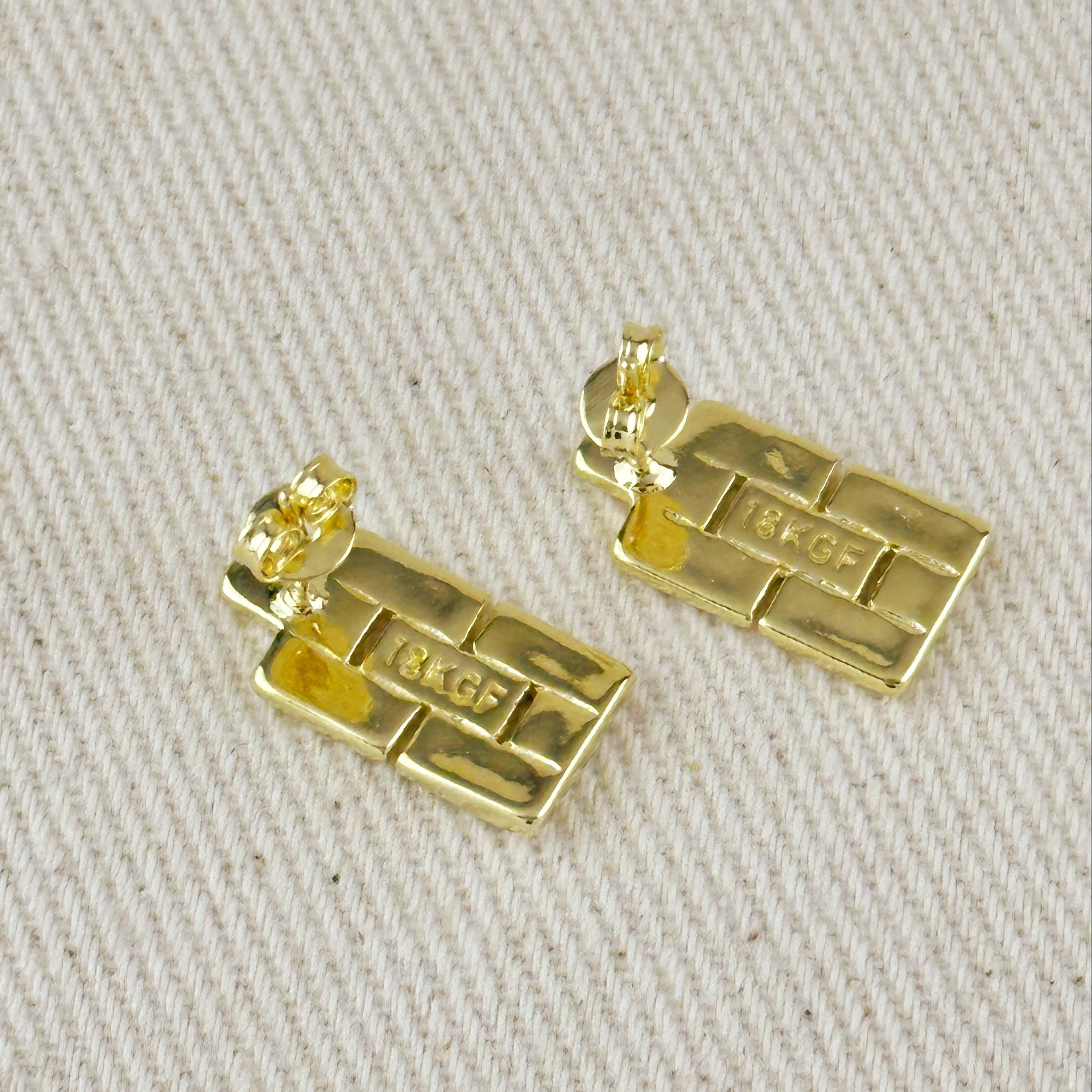 Gold bar-shaped earrings on a beige fabric background