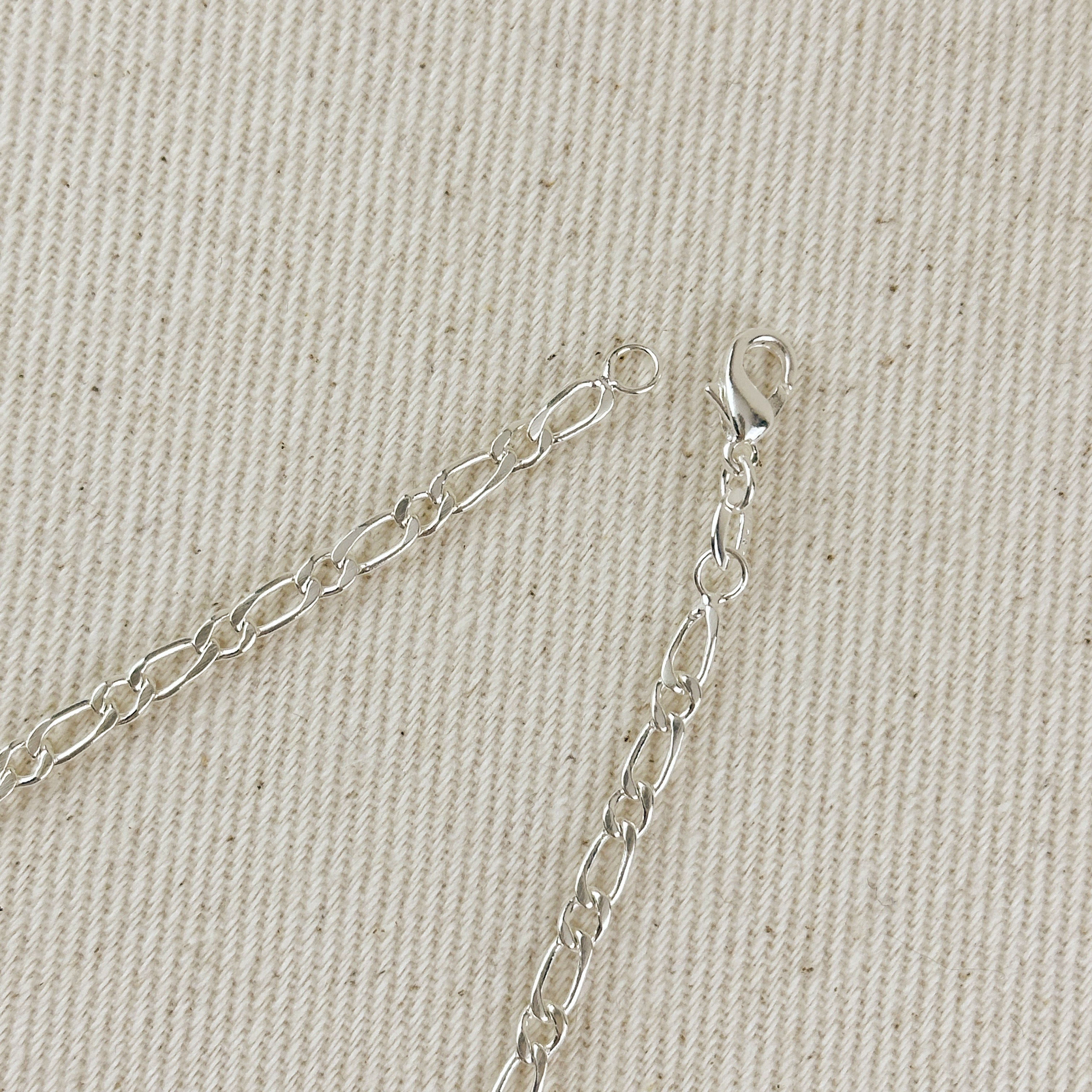 Silver chain necklace on a beige fabric background