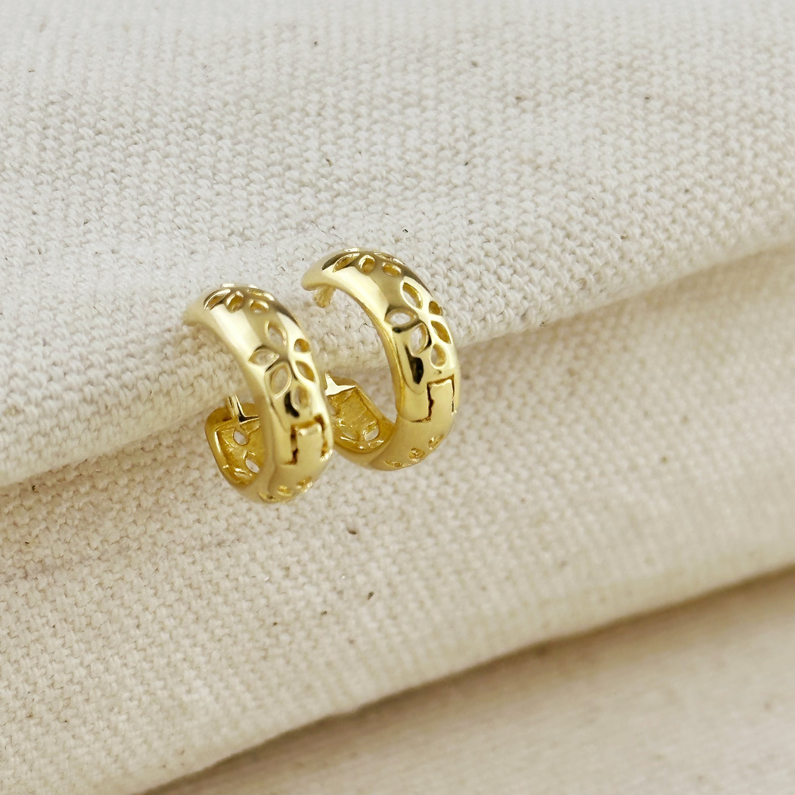 18K gold filled huggies earrings with leaf detailing on a soft fabric background.