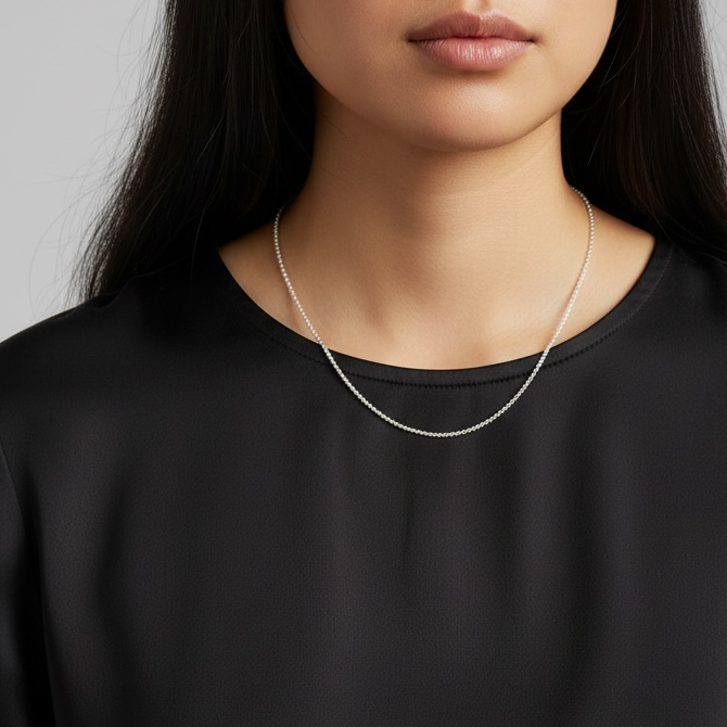 Woman wearing a black top and a delicate necklace against a gray background