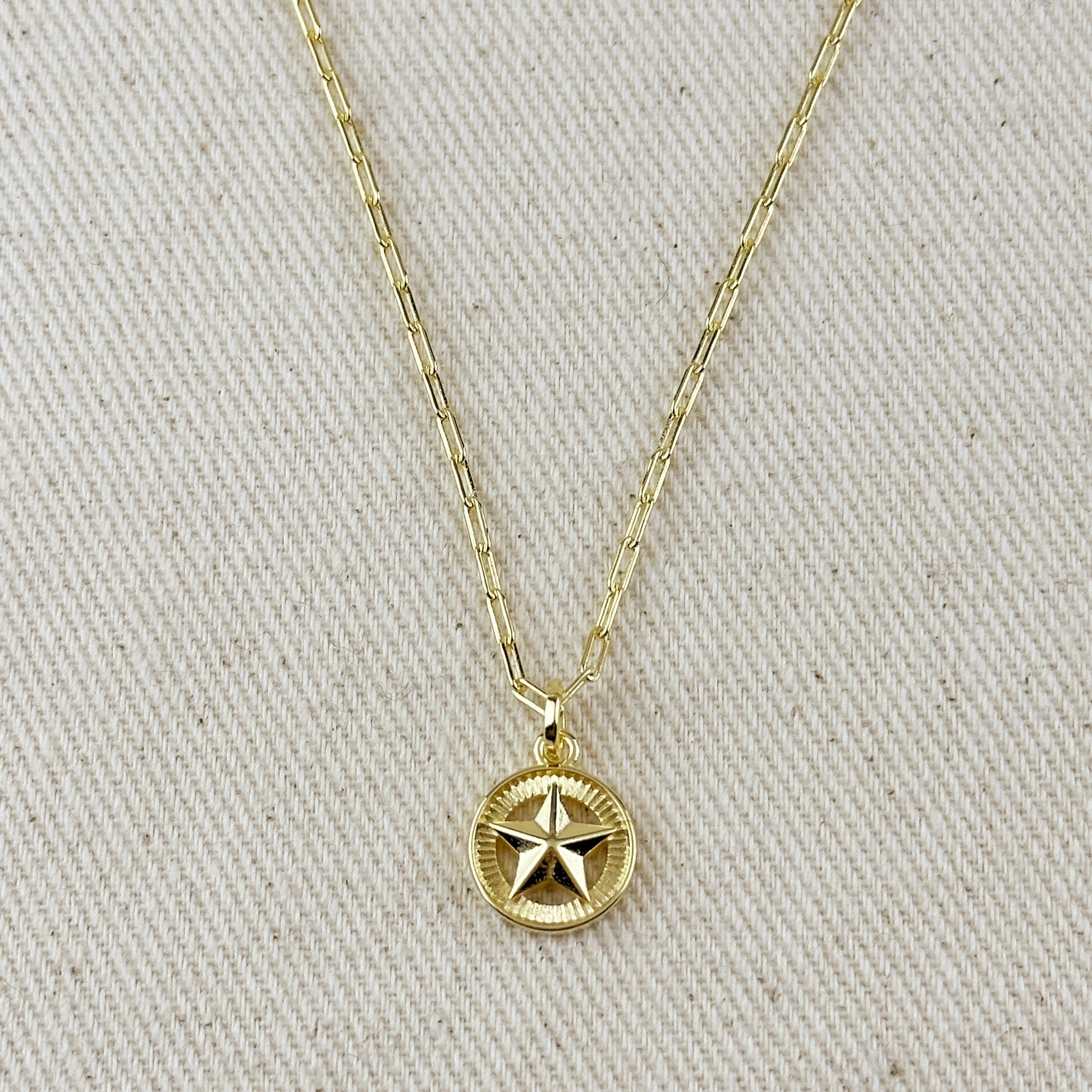 Gold necklace with a star pendant on a beige fabric background