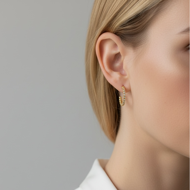 Close-up of a person wearing gold hoop earrings against a neutral background