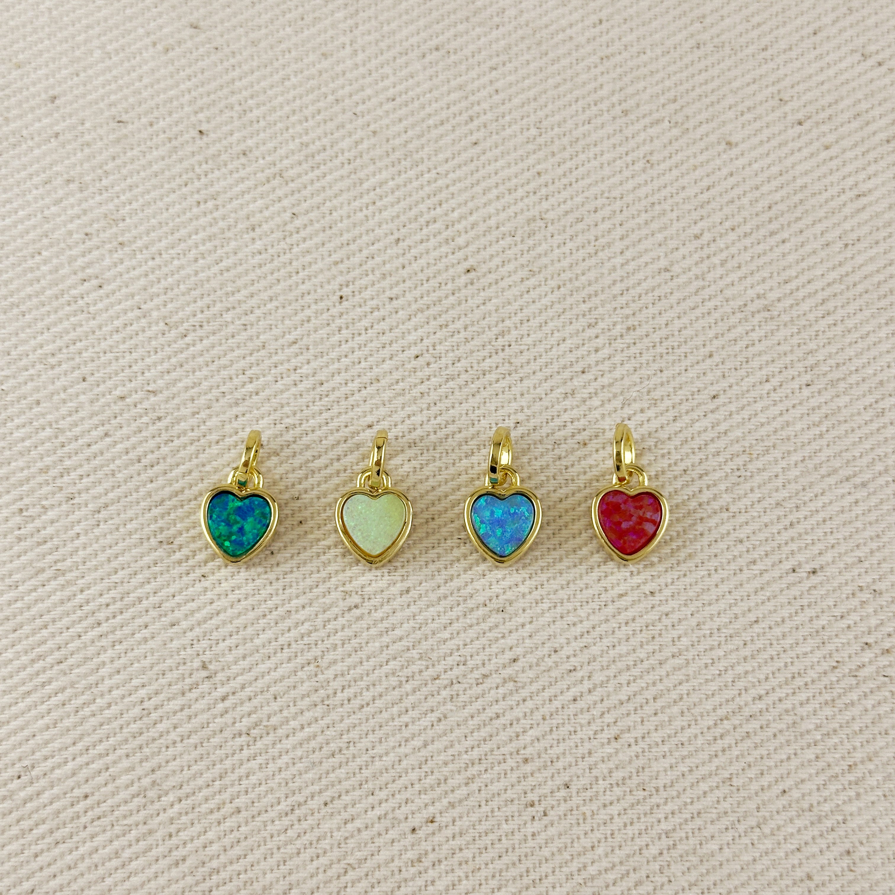 Four heart-shaped pendants with colorful stones on a beige fabric background